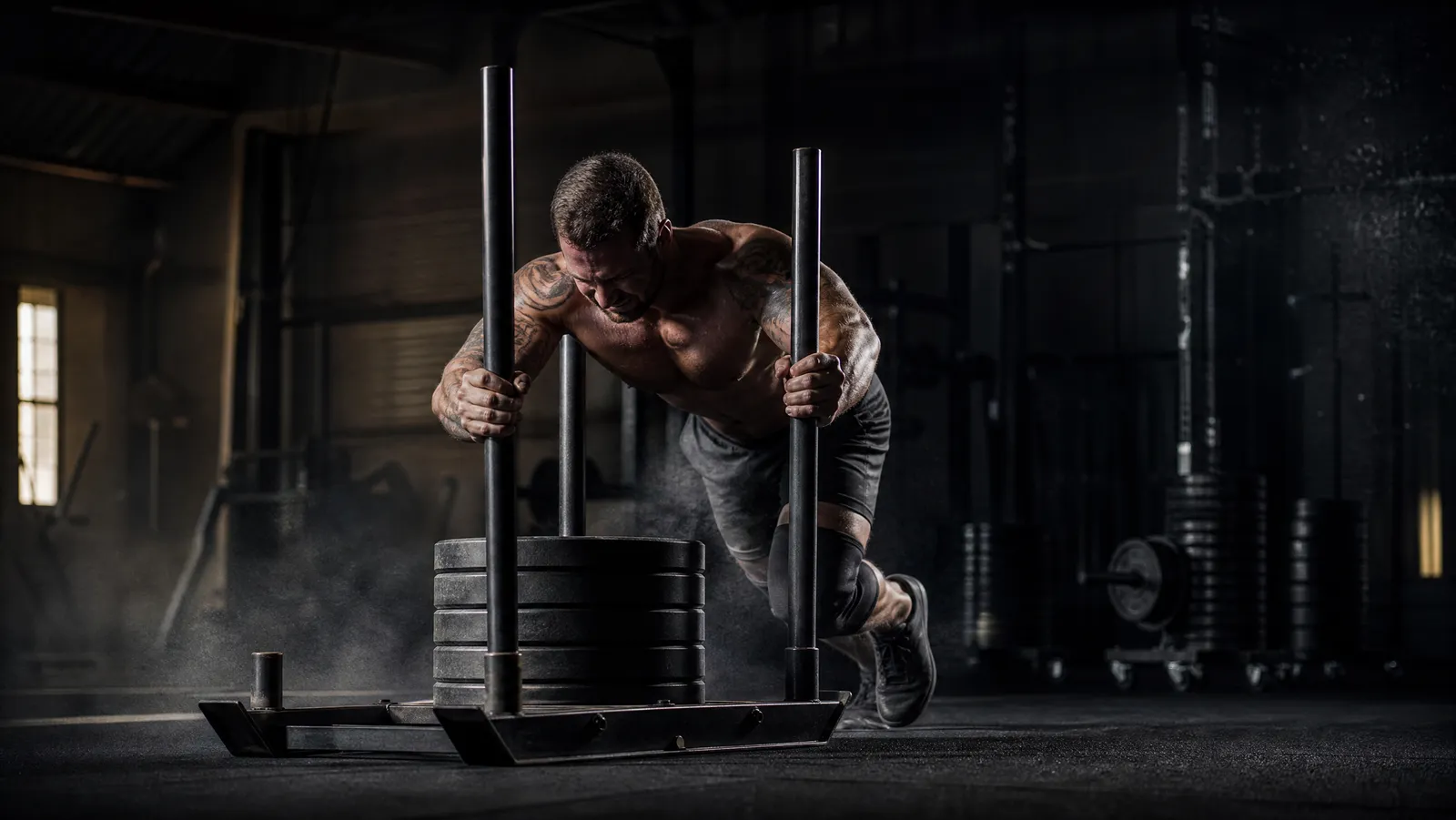 Athlete pushing a weighted sled in a moody home garage gym